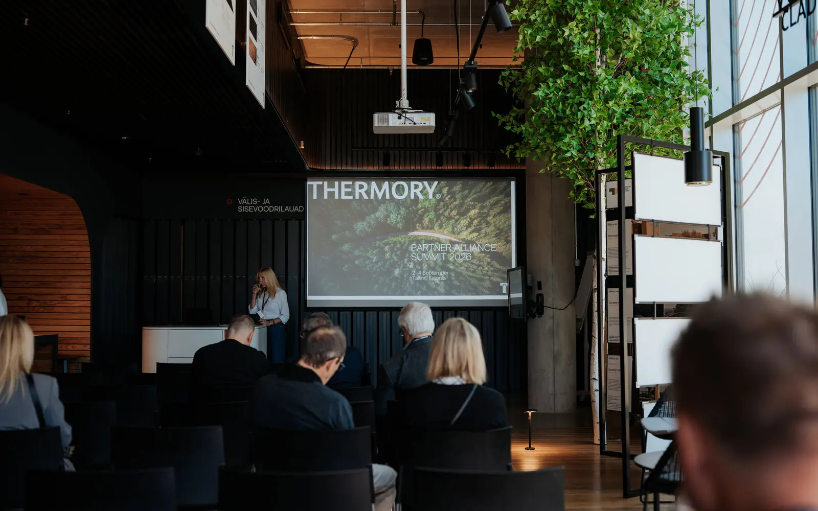 Istuva yleisö katsoo valkokangasta, jossa lukee Thermory Partner Alliance Summit 2026, kun puhuja avaa tilaisuuden