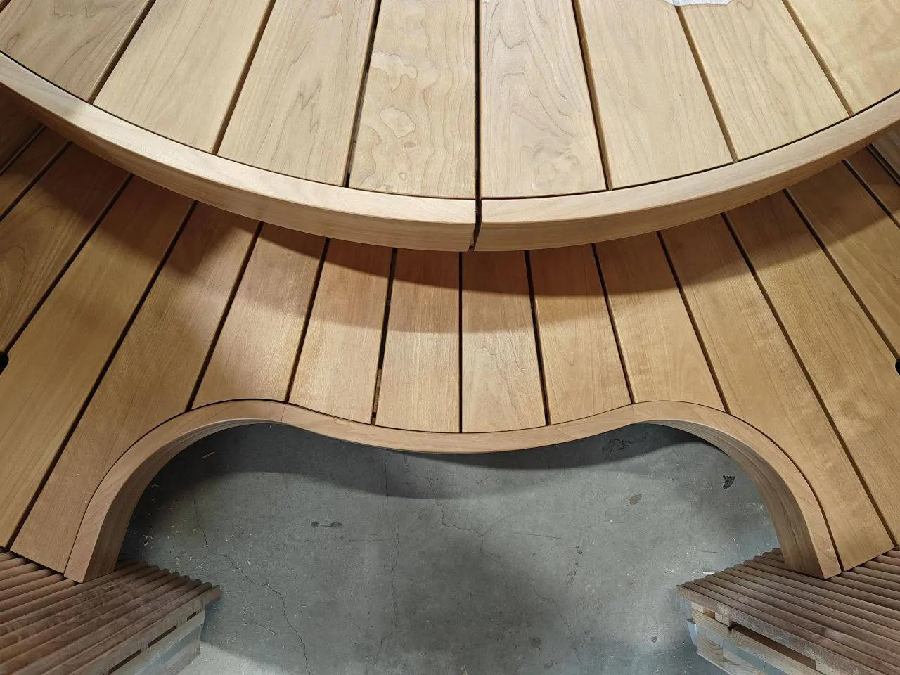 A circular sauna bench of curved wooden slats with a lighting channel under the top tier, on the factory floor at Auroom in Tartu, Estonia.