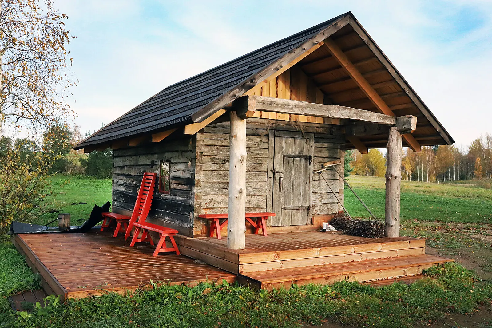 A traditional Estonian log smoke sauna with a black-tarred roof and a wooden deck, in autumn
