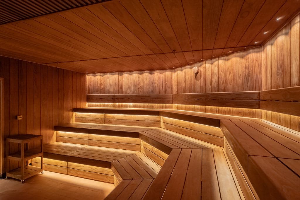 Large-scale commercial sauna with tiered wooden benches and warm ambient lighting