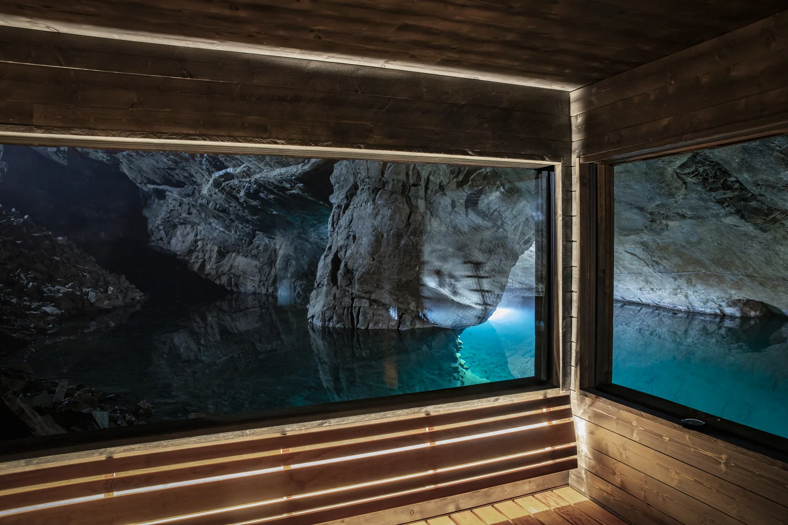 Underground lake and rough rock seen through two sauna windows above a wooden bench