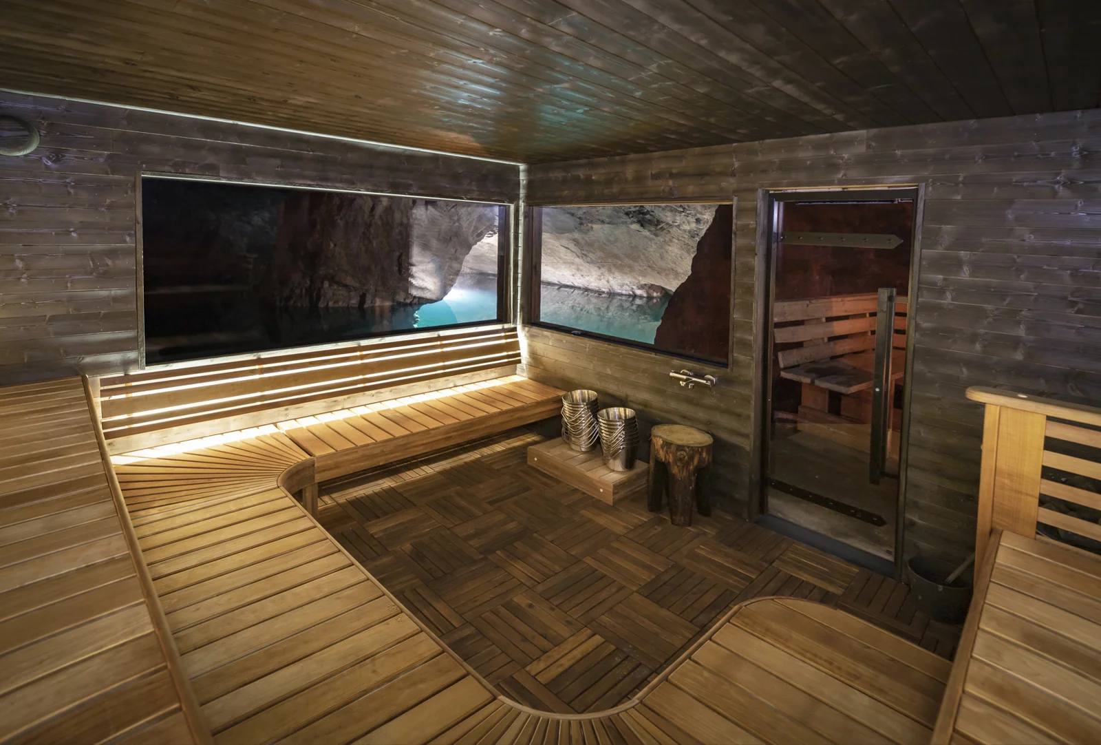 Wooden benches and two large windows looking onto rock and an underground lake inside Adventuremine sauna