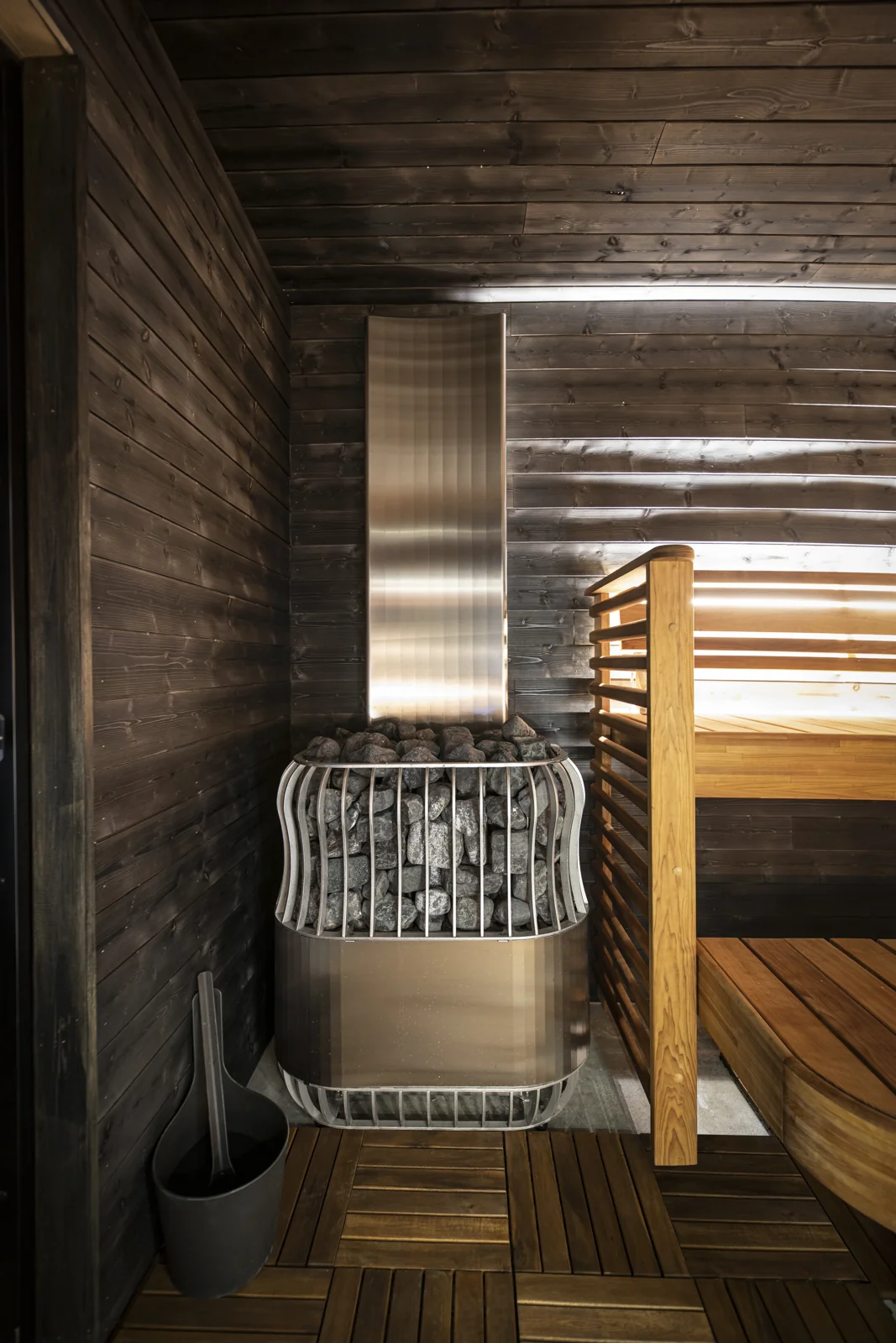 Saunum heater with a basket of stones and tall air duct beside wooden benches