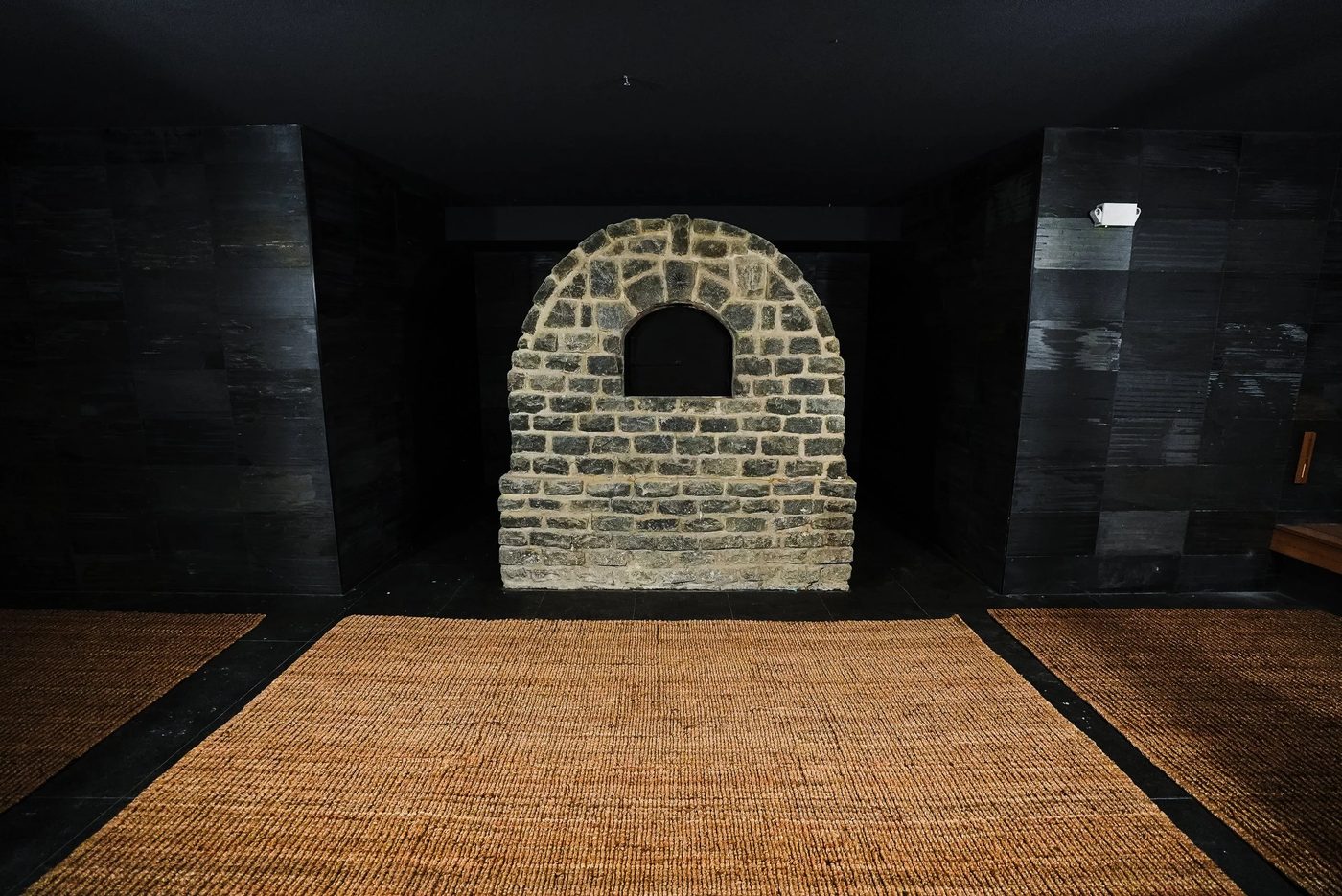 Banya entrance at Bathhouse Atlantic Avenue, Brooklyn, featuring a stone furnace arch in a dark wood-paneled antechamber ahead of the May 16, 2026 opening