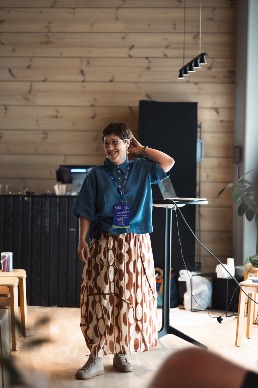 Becky Pelkonen, smiling, standing beside a laptop stand in a pine-paneled room at the World Sauna Forum