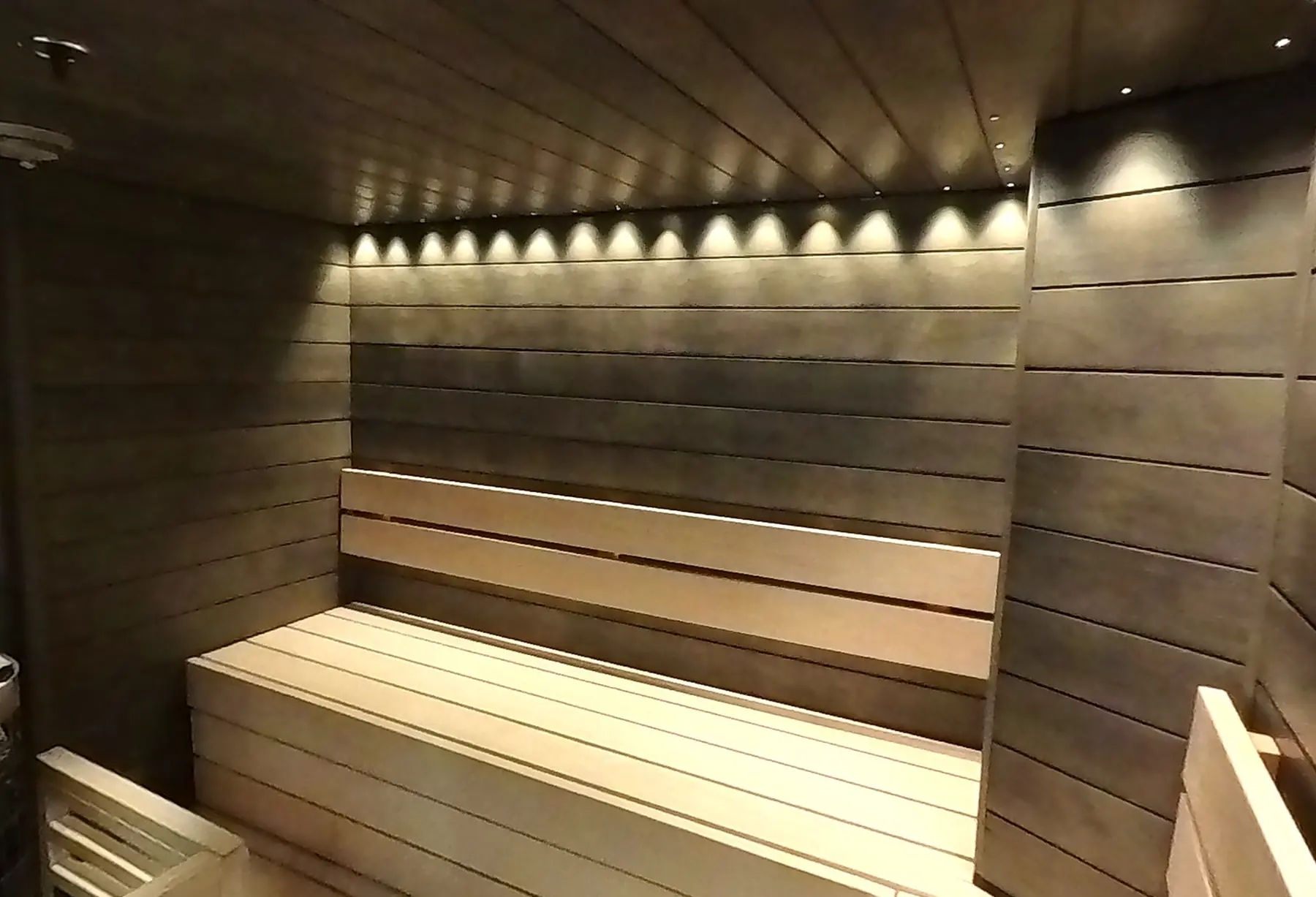 Empty timber benches beneath a row of wall lights in the shared sauna at Lapland Hotels Bulevardi