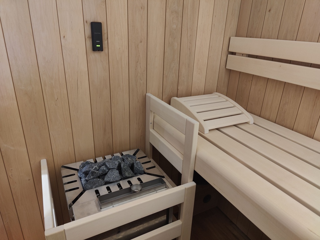 A small black DIATRON OSU-400 module with a green light on a light wood sauna wall above an electric heater and benches
