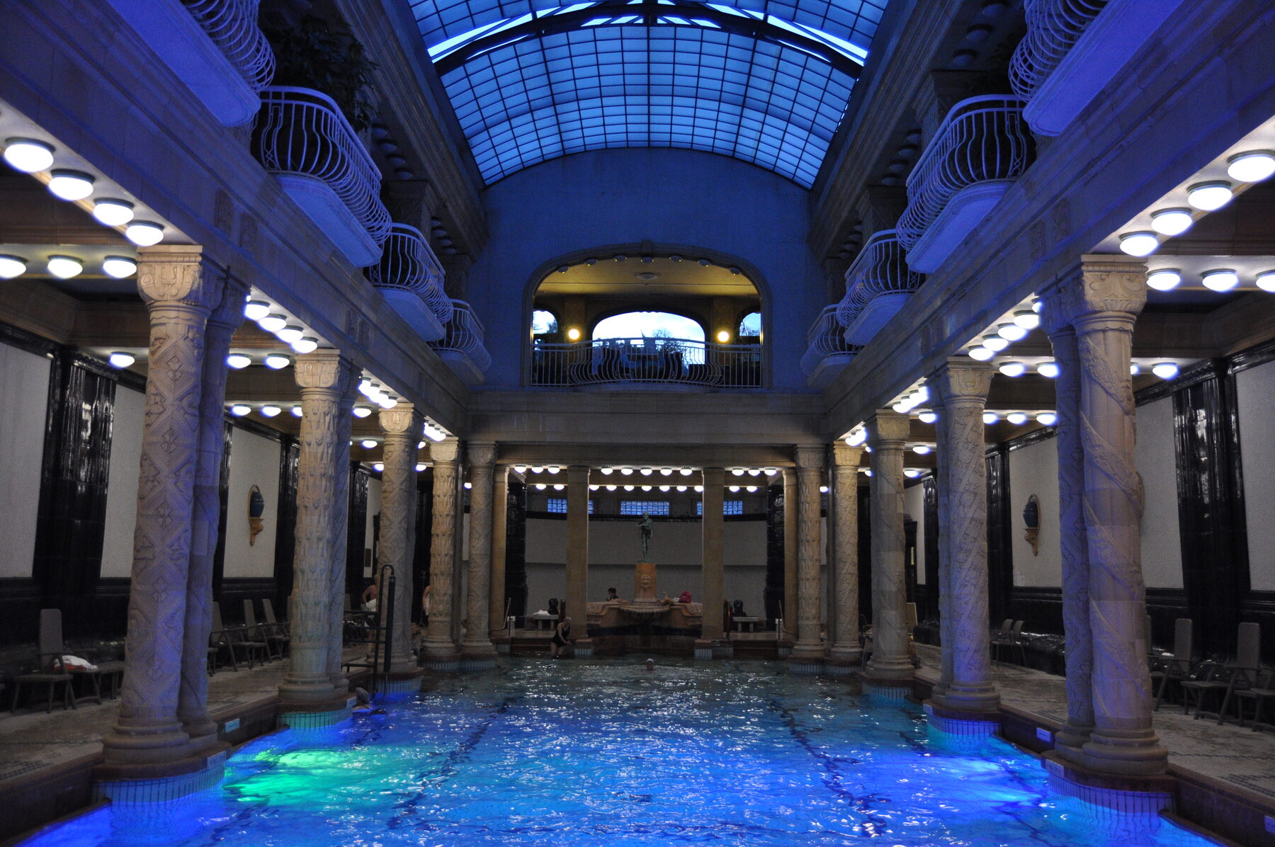 Columned indoor pool hall with a glass barrel roof and balconies at the Gellért Baths in Budapest