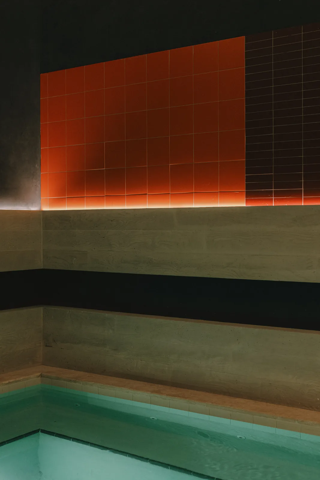 A wall of orange and dark tile above stone ledges and a turquoise pool