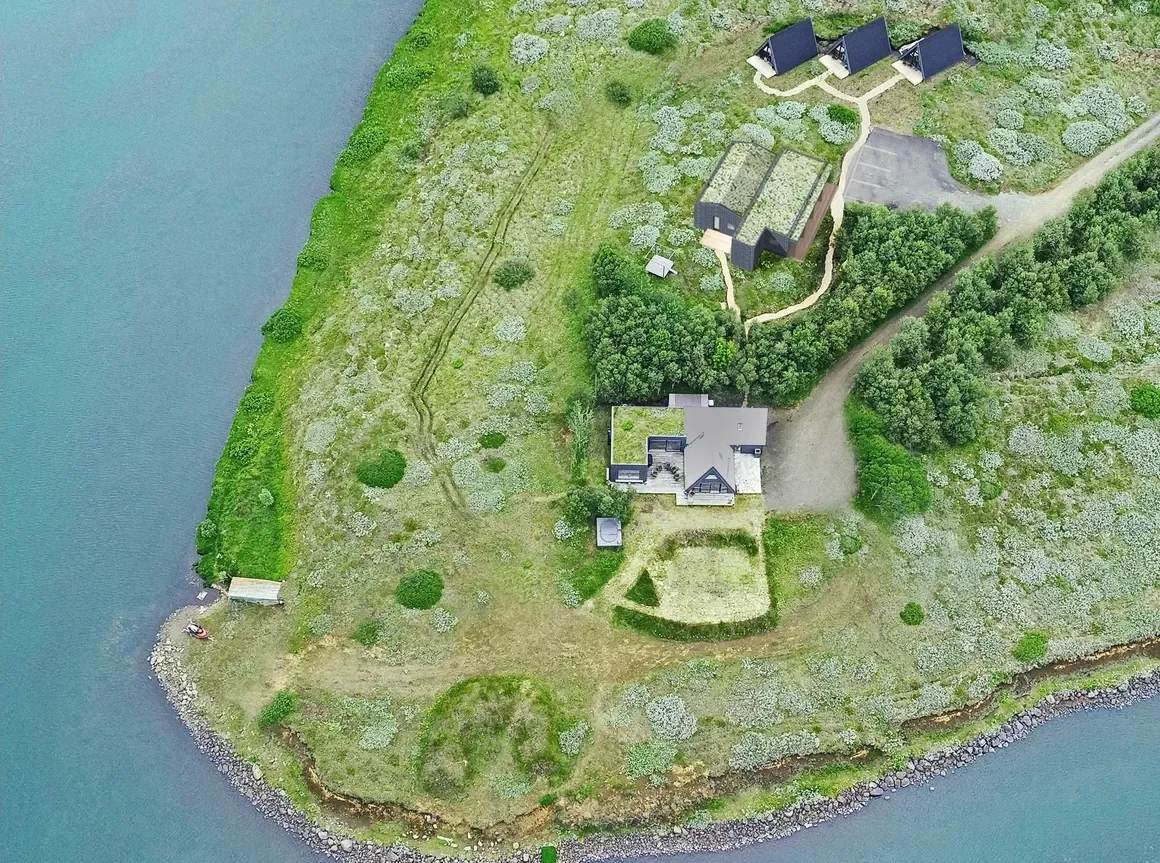 Aerial drone view of the wooded peninsula on Lake Gíslholtsvatn in southern Iceland showing the 10-bedroom lakefront lodge and outbuildings surrounded by water on three sides