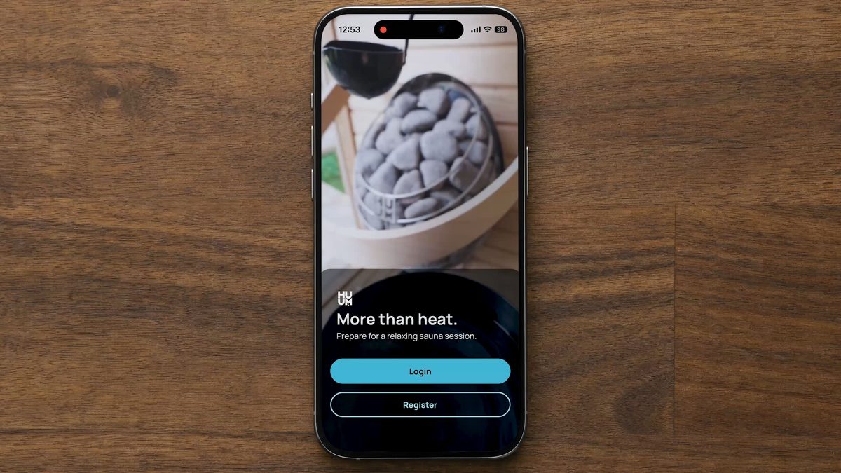 iPhone showing the HUUM App 4.0 login screen with More than heat tagline on a wooden table