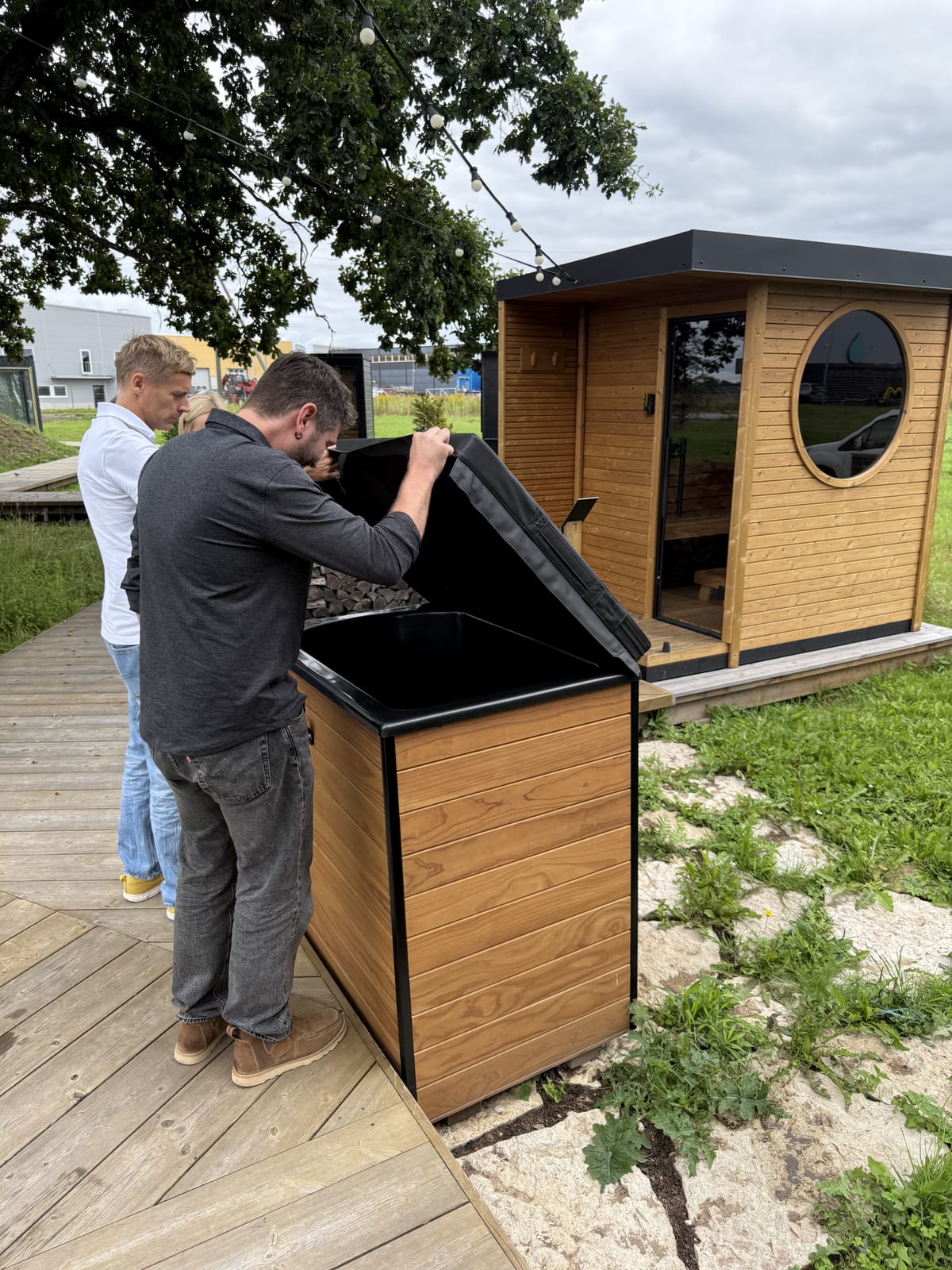 Ben Frizzell lifts a cold plunge cover beside a man in a white shirt at HUUM’s outdoor showroom.