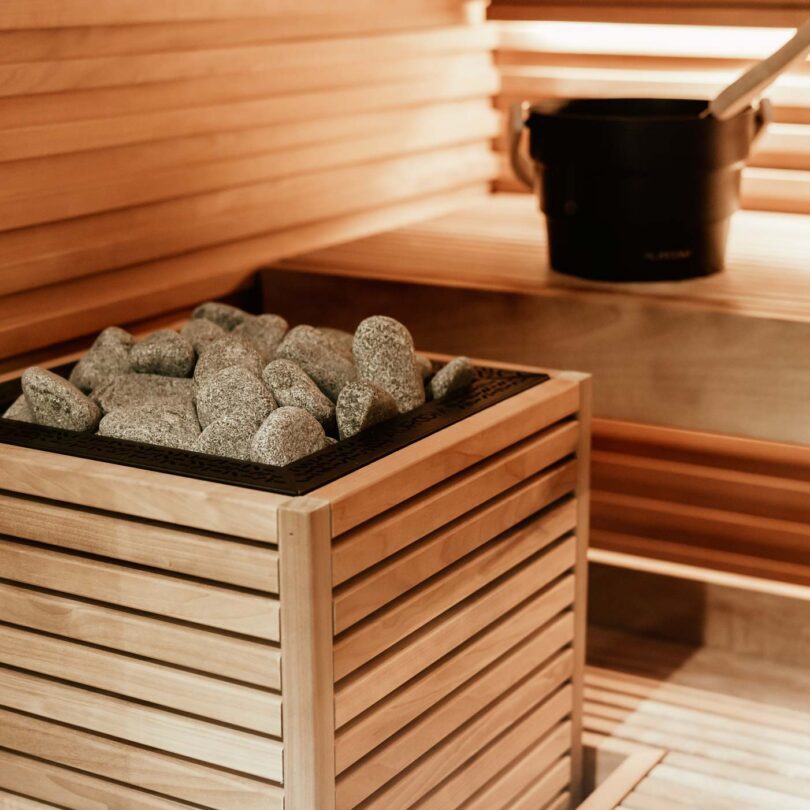 HUUM Core electric heater clad in slatted wood panels, stones visible at the top, inside a sauna