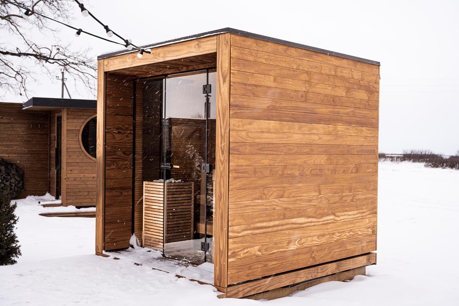 An outdoor sauna in winter snow, with a HUUM Core electric heater visible through its glass front