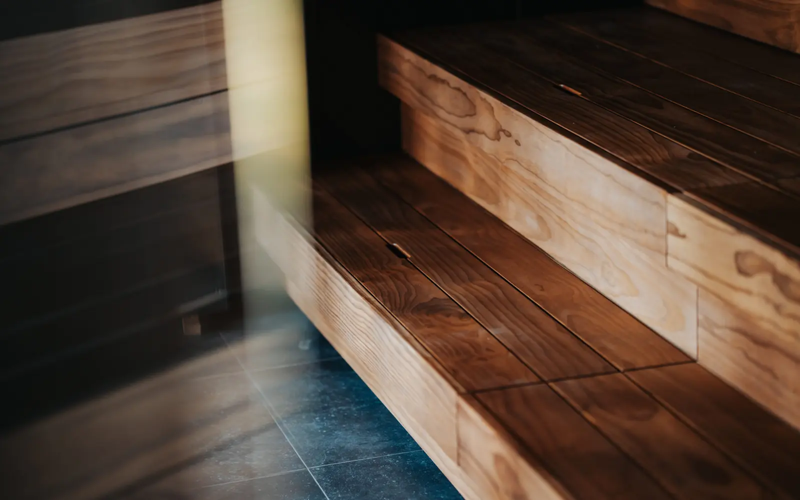 Two broad wooden sauna bench steps above a dark tile floor