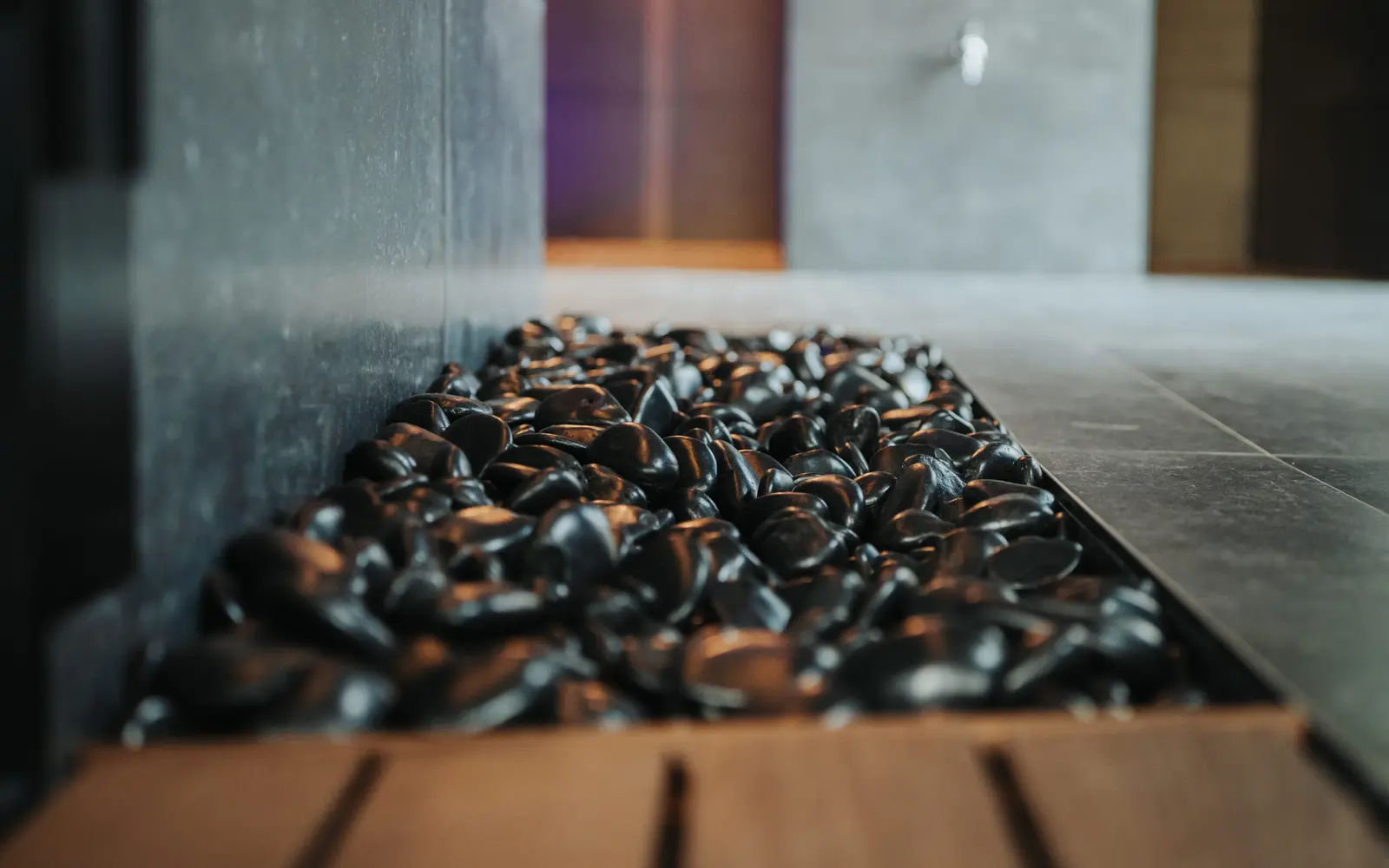 A long bed of dark stones set in a wooden frame beside a gray stone wall