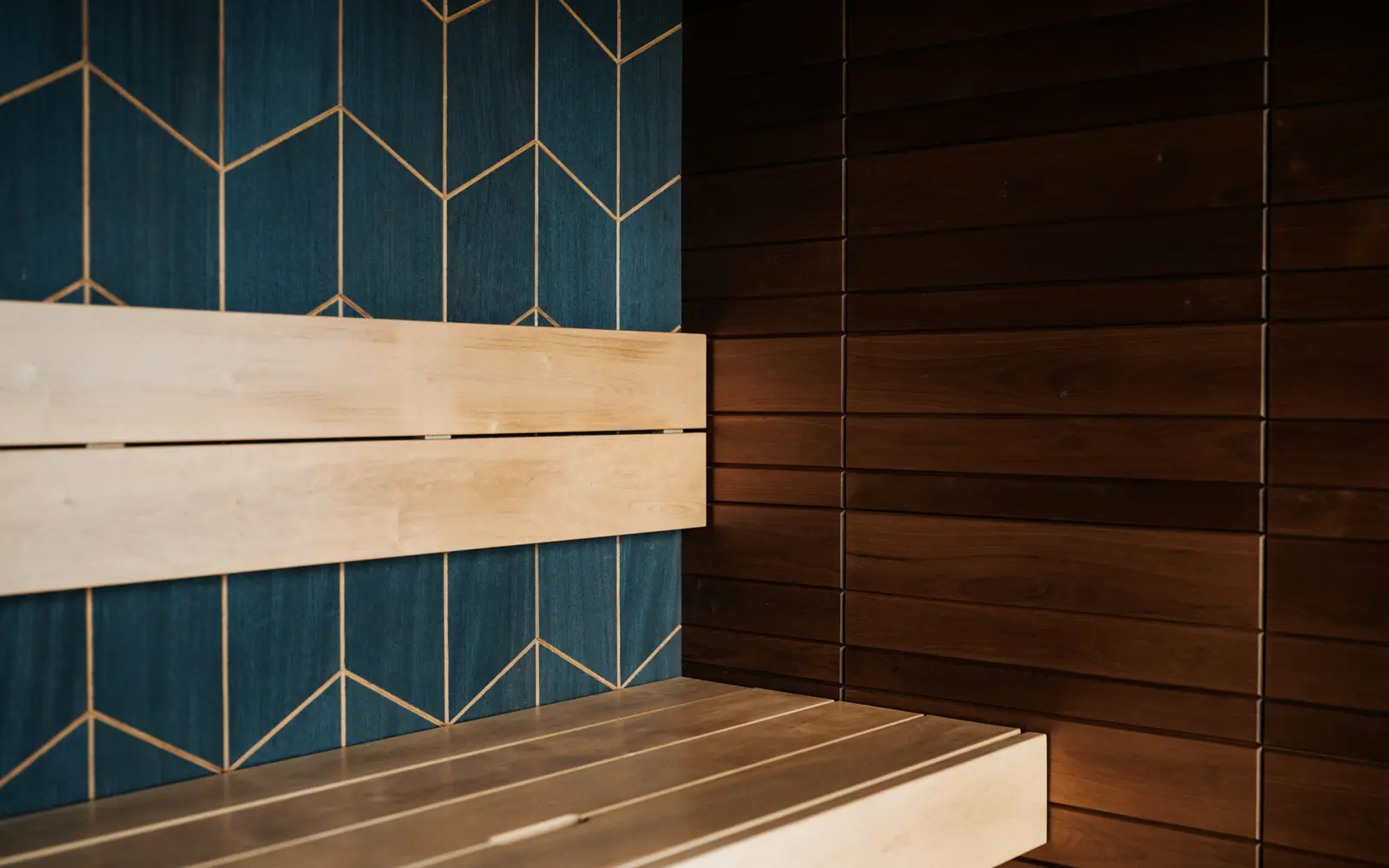 Pale wooden sauna benches against a dark blue wall with a gold geometric pattern and dark wood paneling