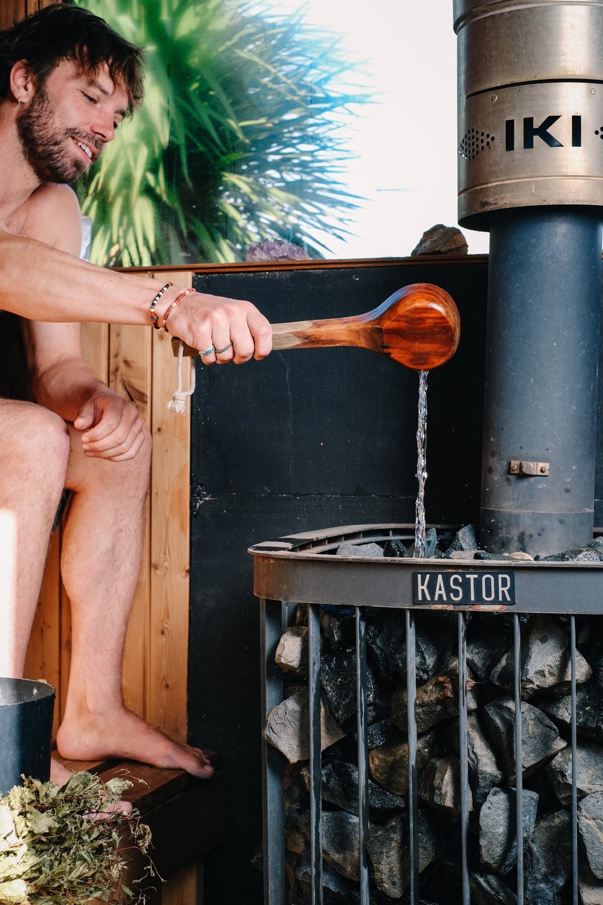 A bather ladles water onto the stones of a wood-burning sauna stove