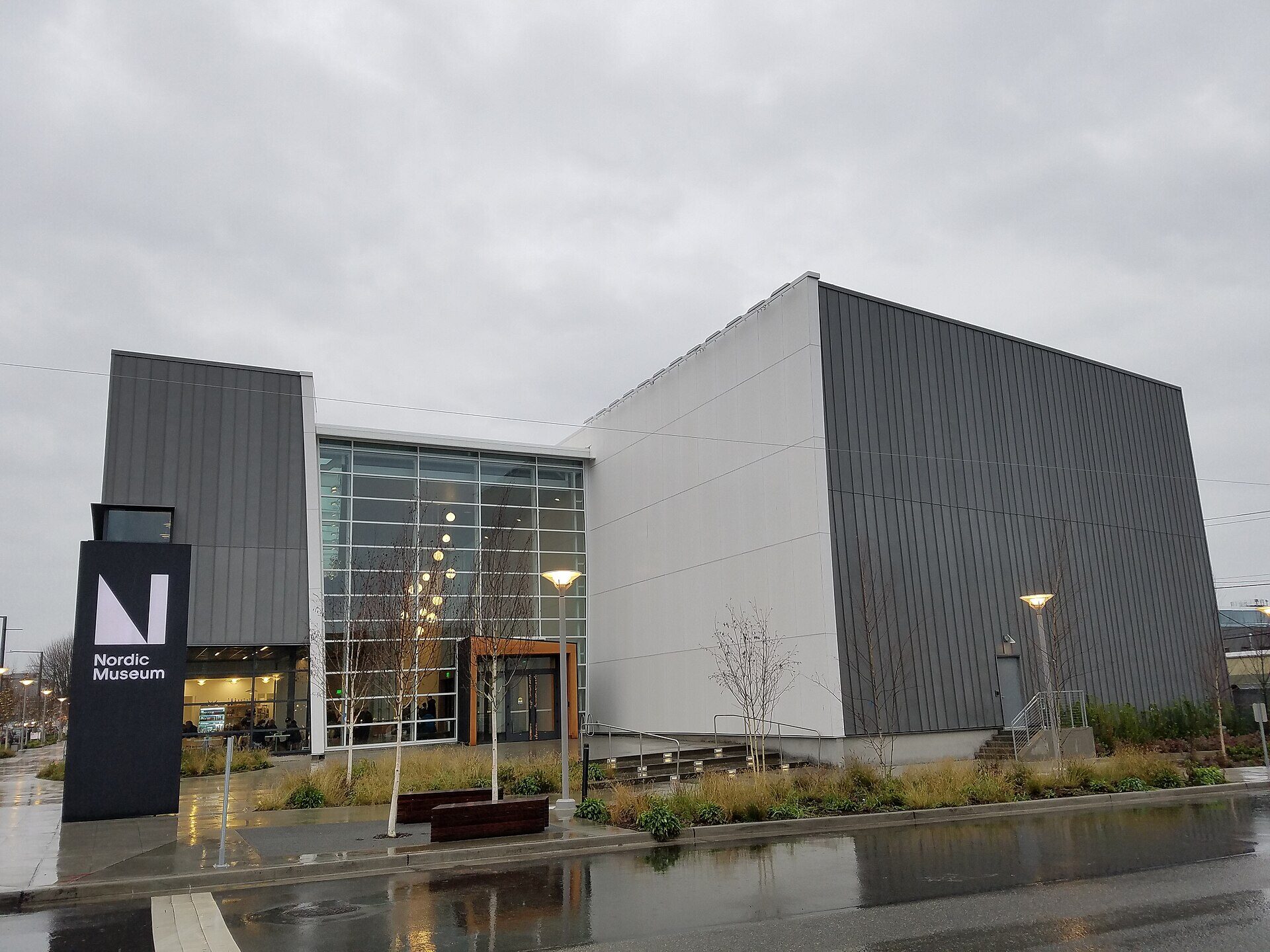 The National Nordic Museum in Seattle, a gray metal-clad building with a tall glass entrance, on a wet overcast day