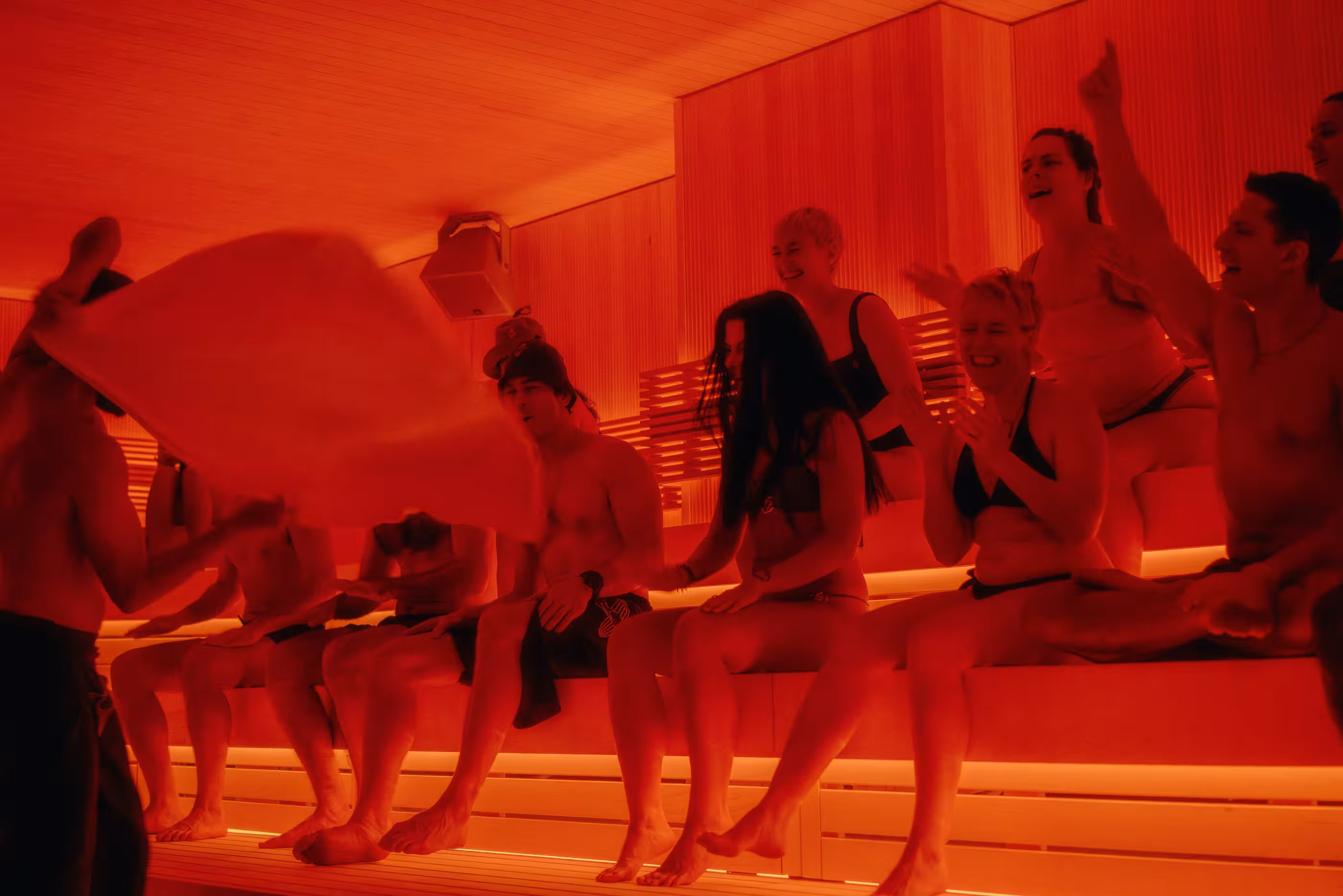 A guide waves a towel in front of guests seated in Othership Williamsburg’s red-lit sauna.