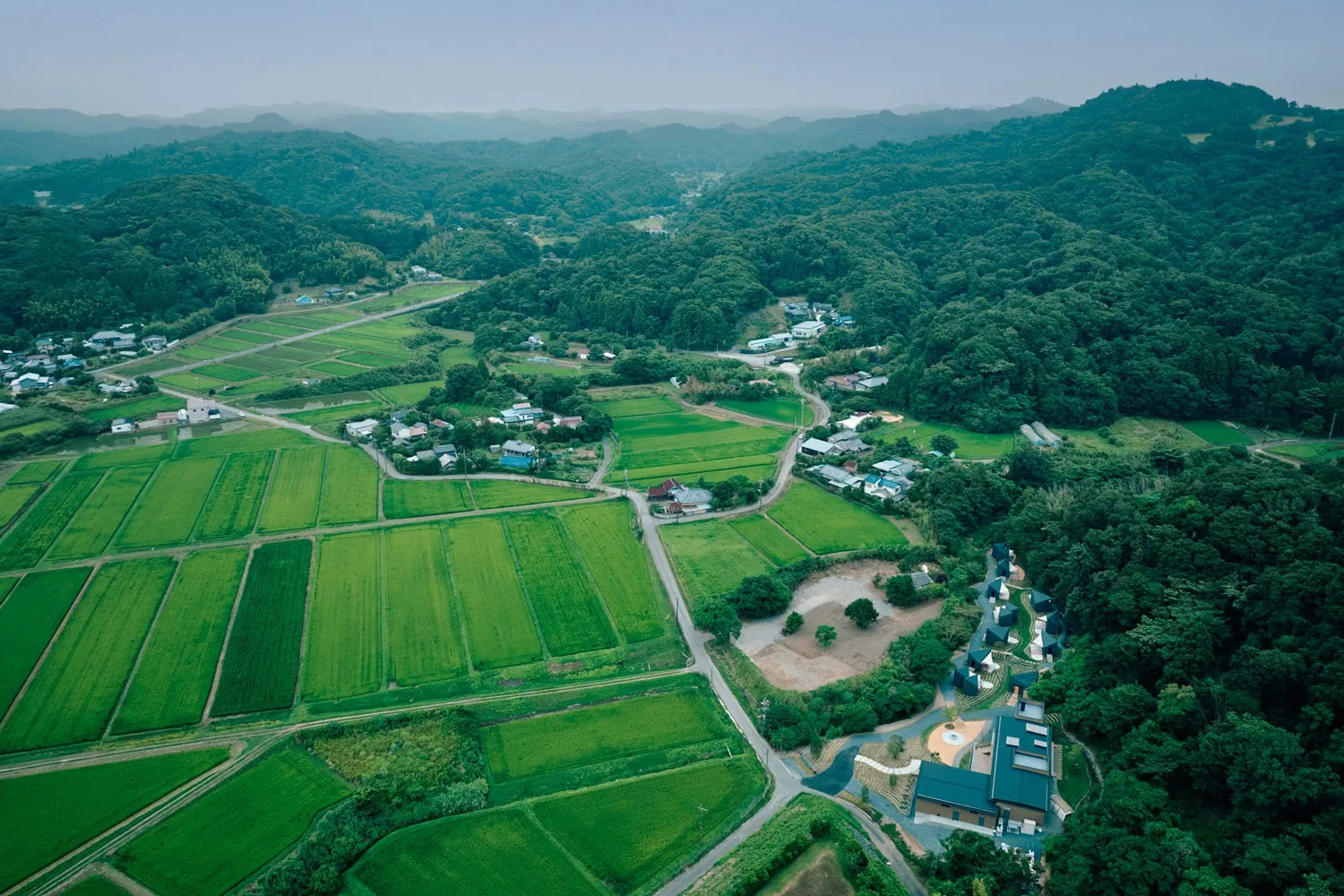 Aerial view of green rice paddies and wooded hills, with the resort's buildings tucked into the trees at the right