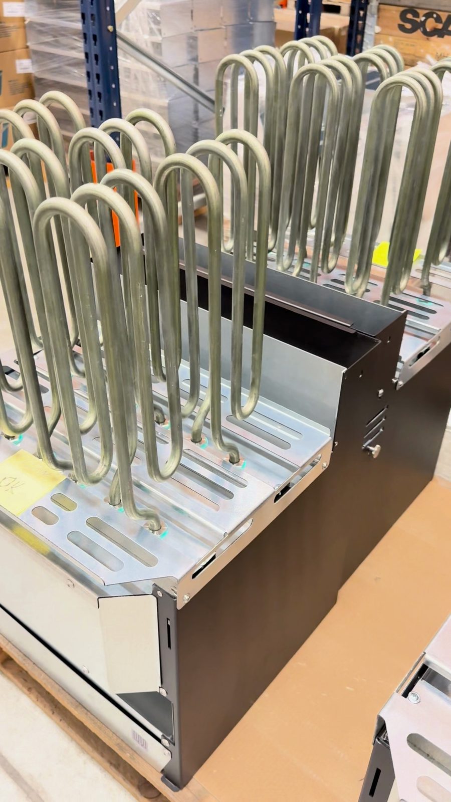 Looped metal heating elements standing up out of open heater bodies on a pallet, with a yellow note marked OK on the nearest