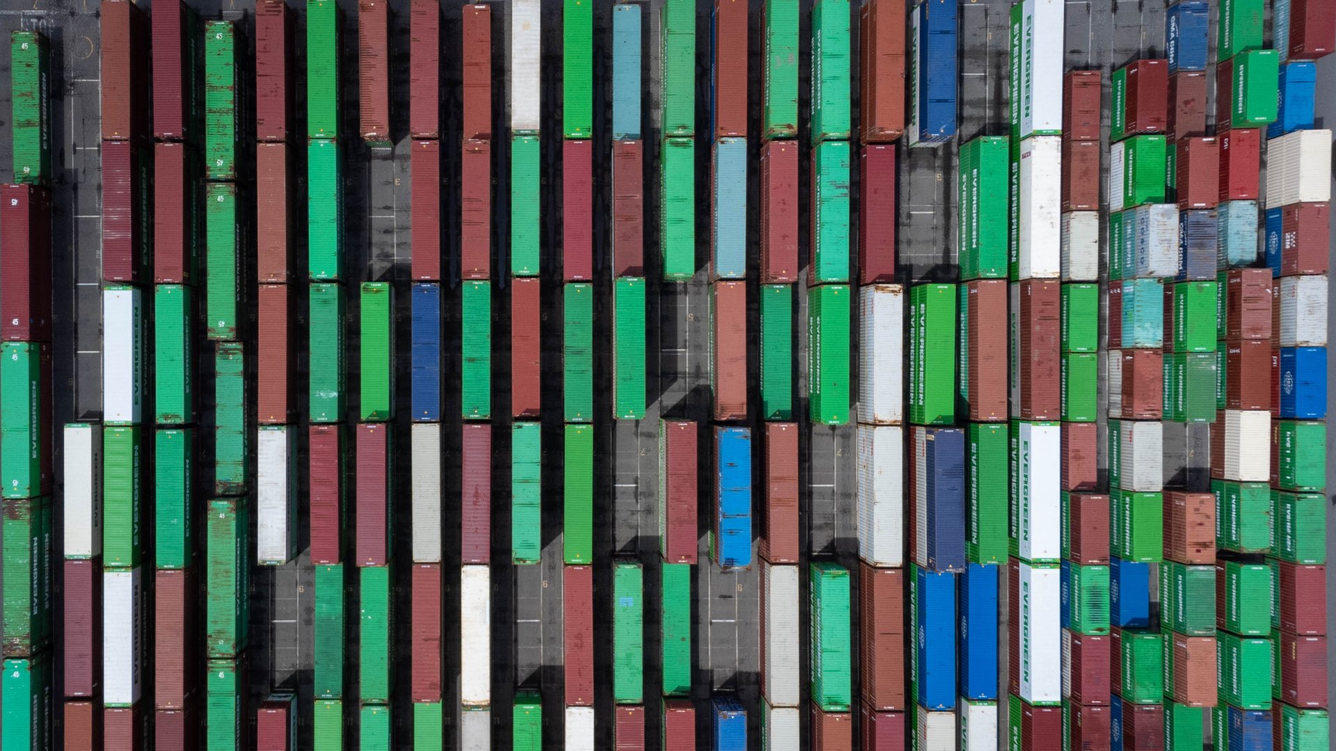 Overhead view of rows of red, green, blue and white shipping containers stacked in a port container yard