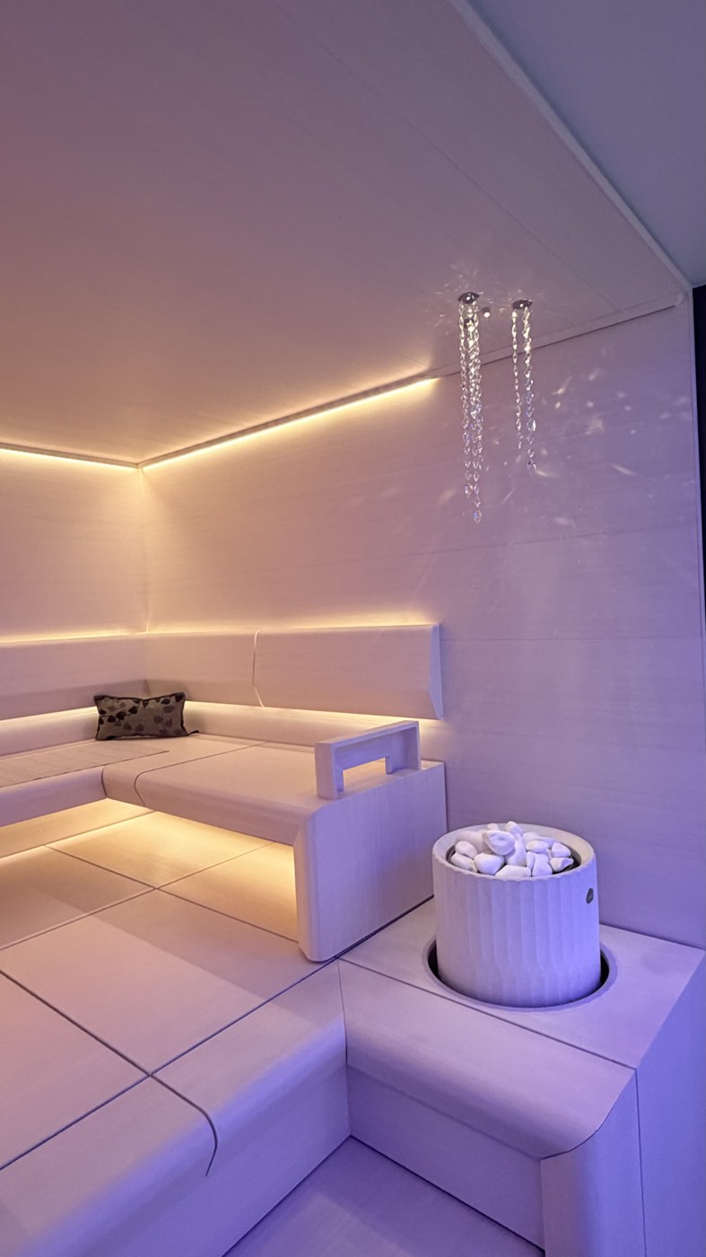 White fluted Tulikivi sauna heater with white stones beside the benches in Cariitti’s white display sauna