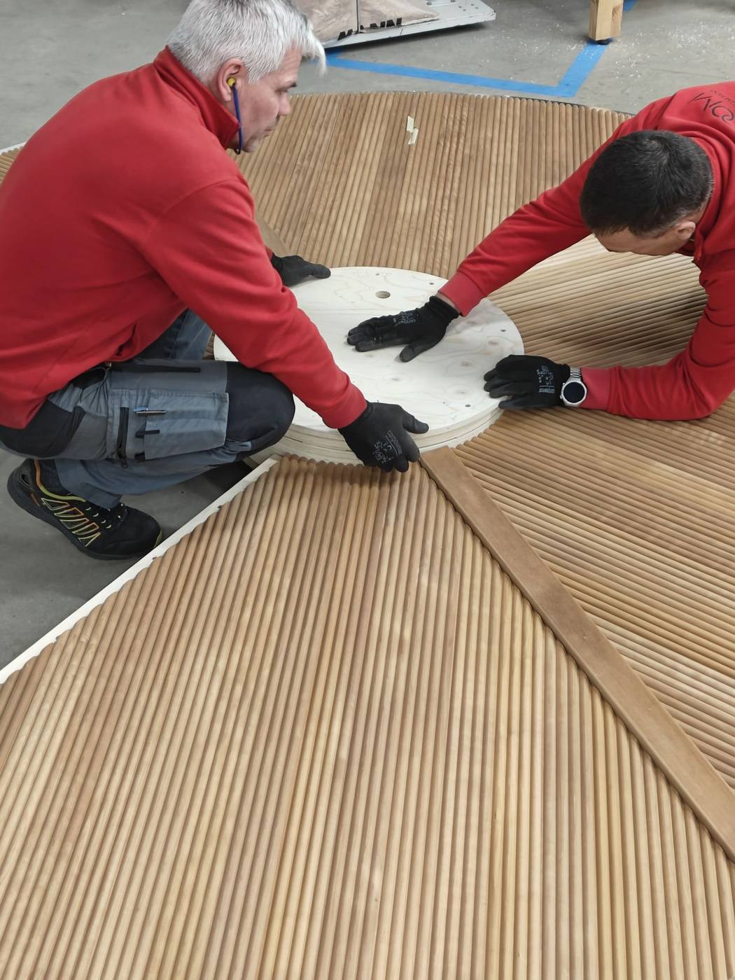 Auroom craftsmen finish curved wooden floor slats around a circular bench piece on the factory floor in Tartu, Estonia