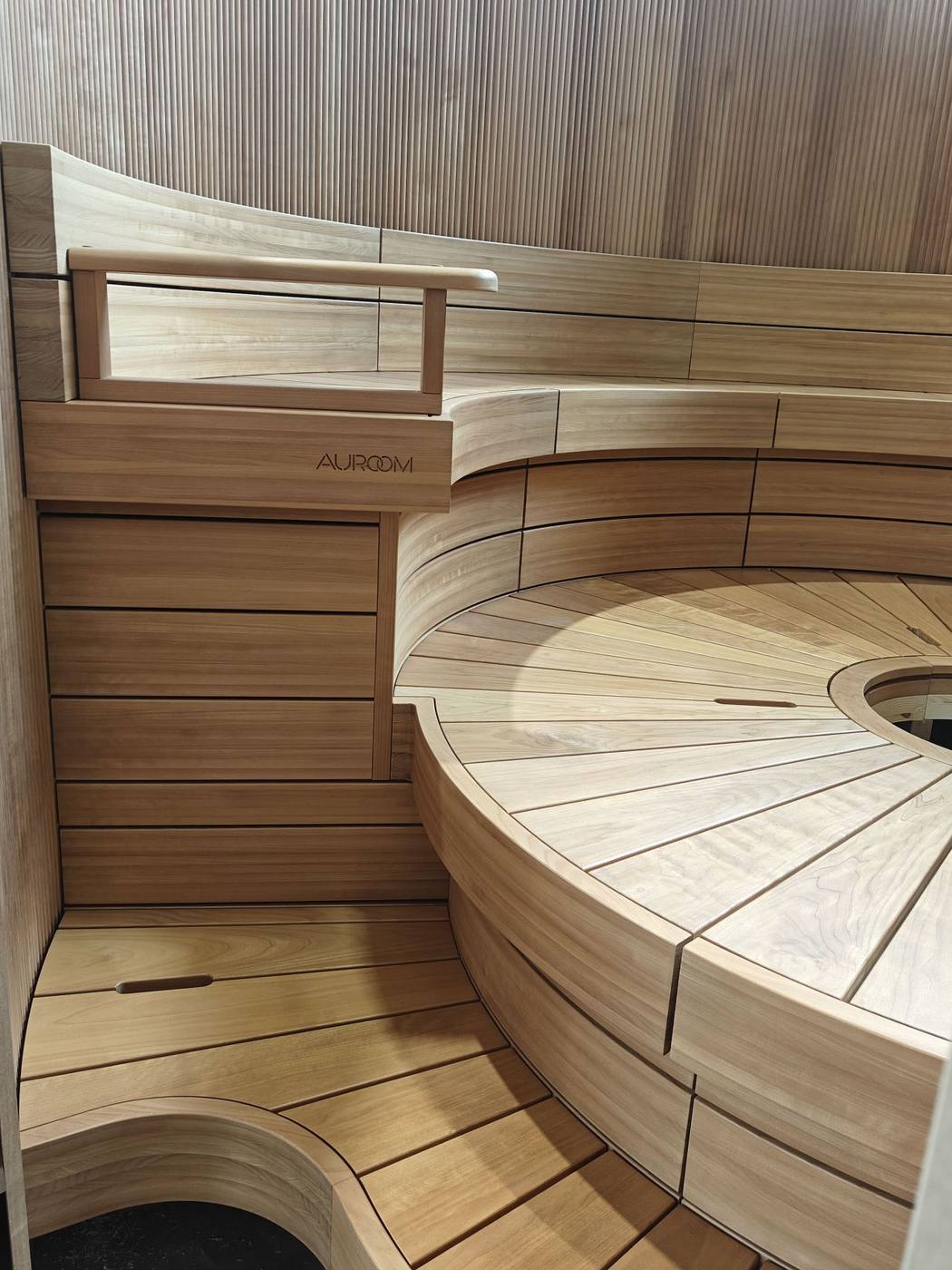 Finished Auroom modular sauna interior with curved tiered benches, branded headrest, and warm cherry wood cladding
