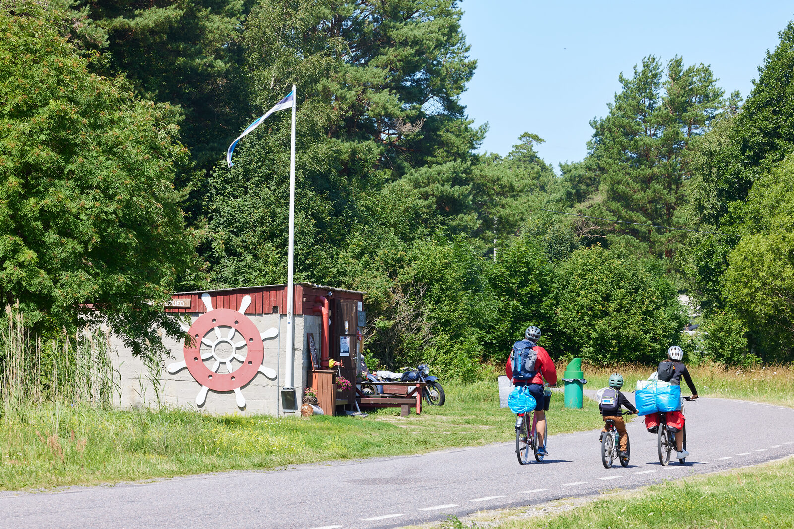Cyclists riding past a shed with a painted ship’s wheel and an Estonian flag on the island of Kihnu